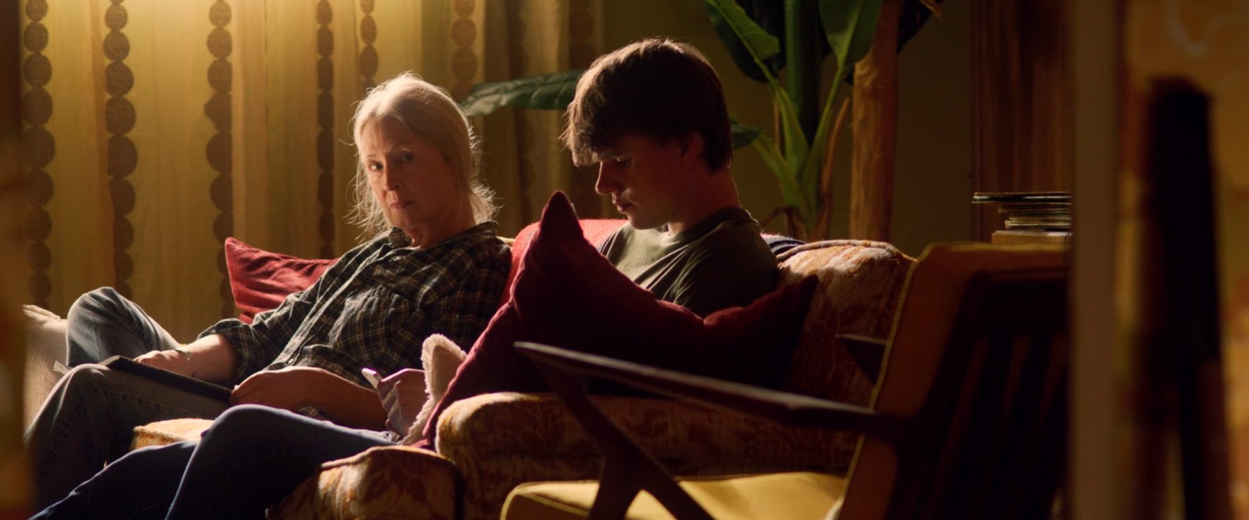 Doris watches Quinn from across the couch in warm lamplight