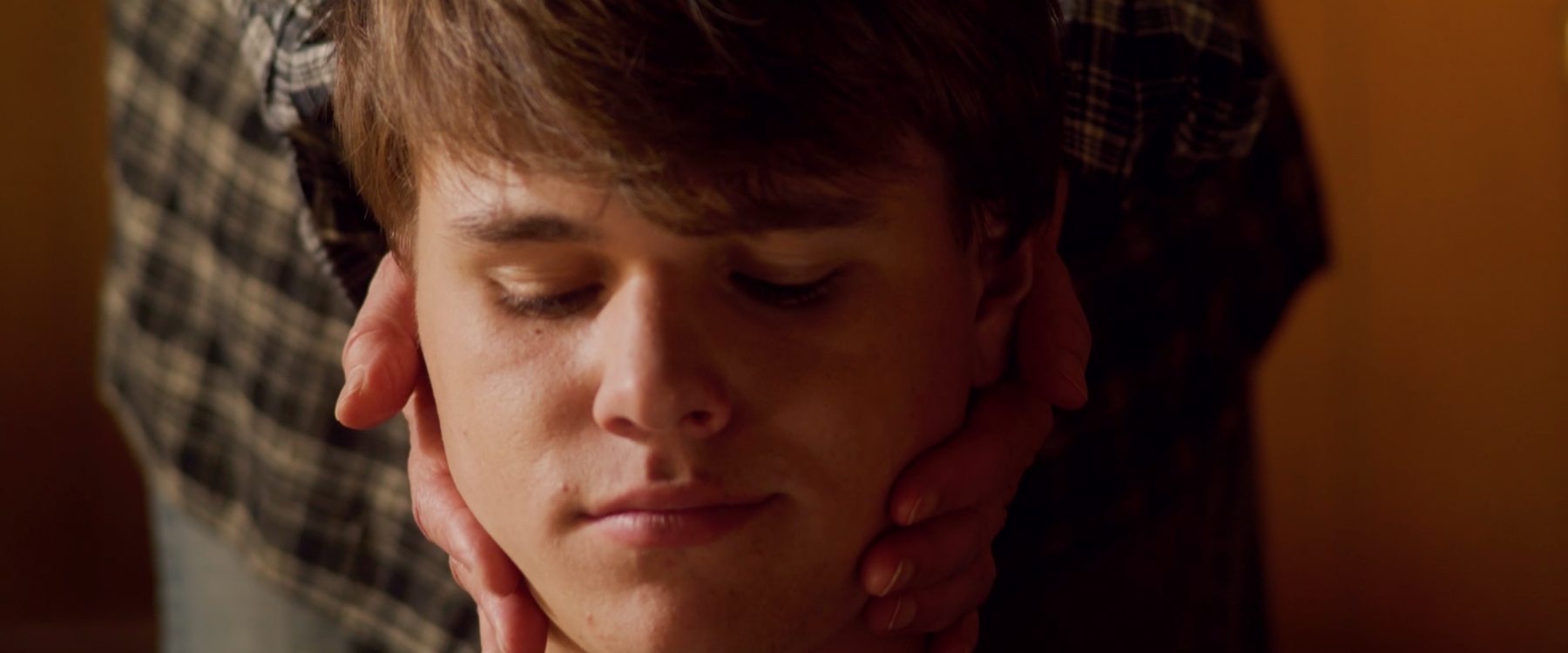 Close-up of Quinn, eyes lowered, Doris's hands cradling his face
