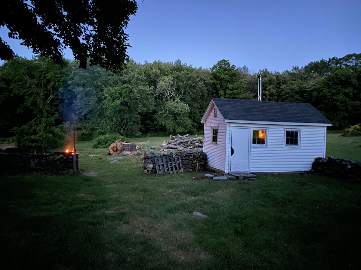 The sugar shack at dusk, a fire burning by the stone wall